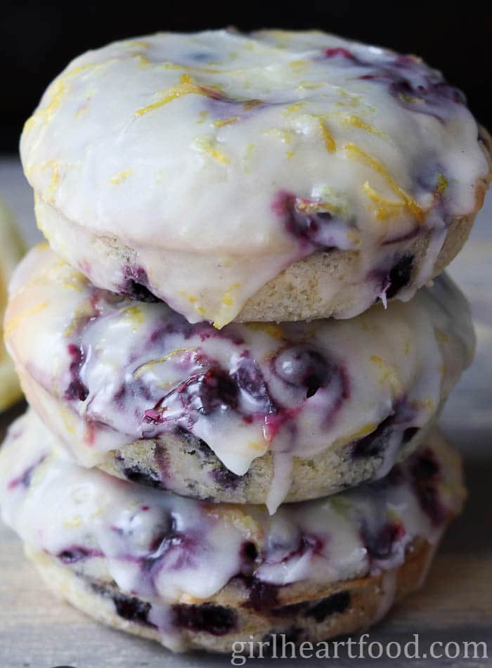 Close-up of a stack of three baked blueberry donuts with lemon glaze.