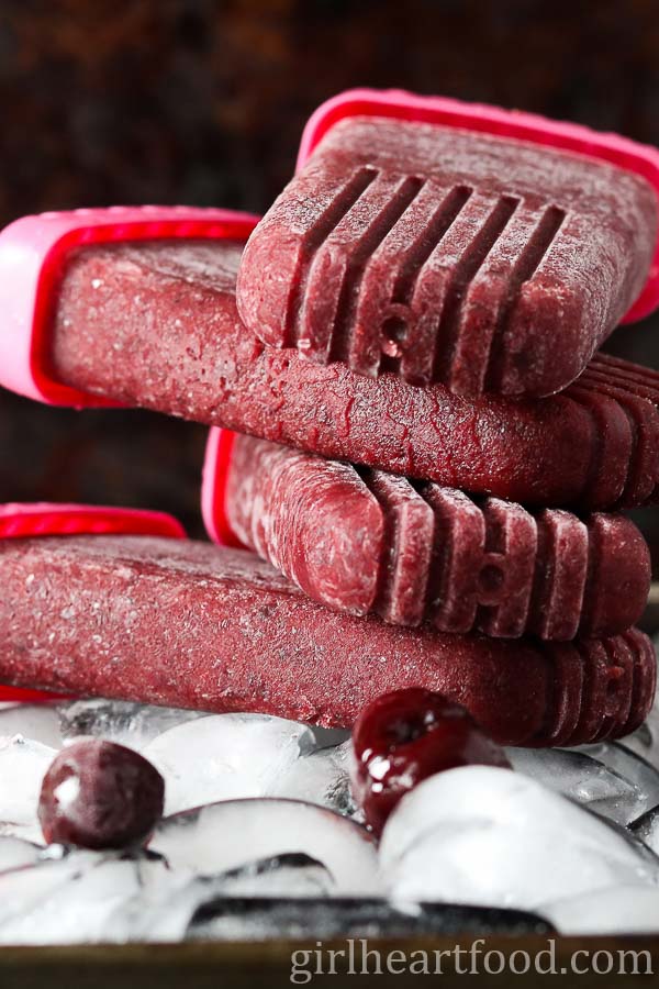 Four cherry vanilla ice pops stacked on a tray of ice cubes.