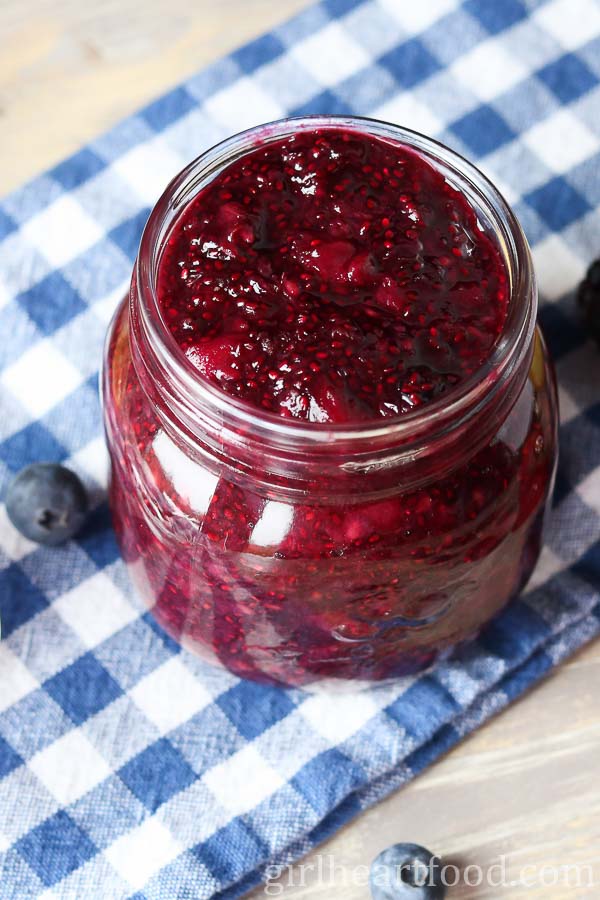 Jar of berry chia seed jam on a blue and white checkered tea towel.