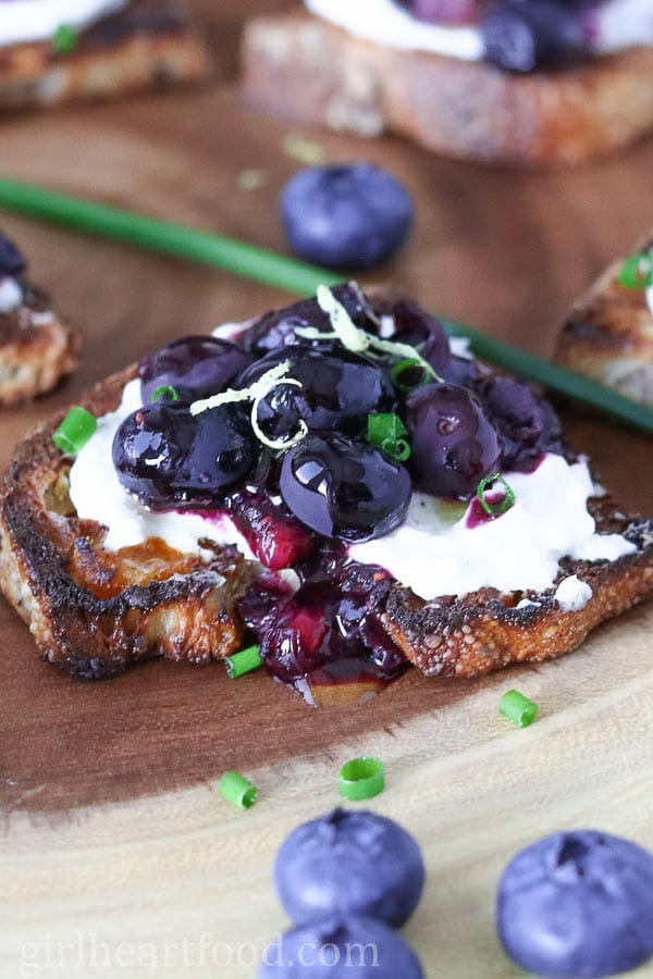 Roasted blueberry and goat cheese crostino next to blueberries and chives.