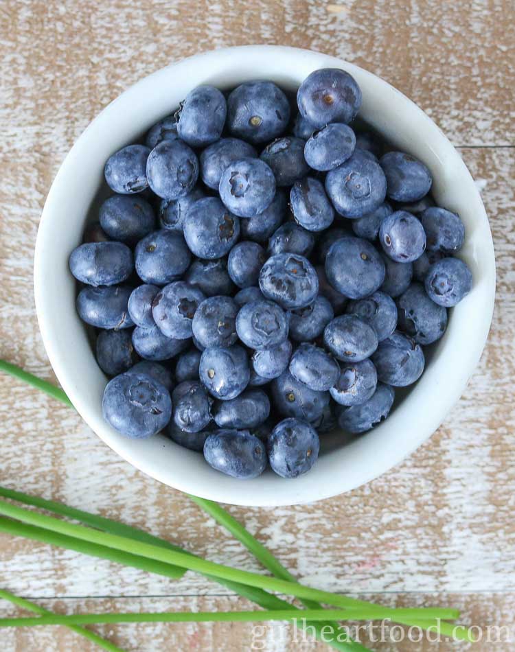 Bowl of fresh blueberries next to some fresh chive sprigs.