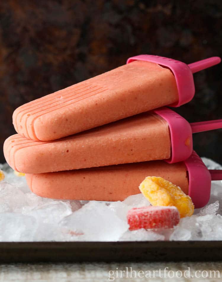 Three frozen fruit ice pops stacked on a tray of ice.