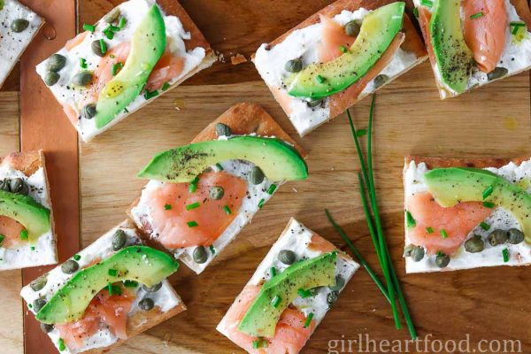 Avocado and smoked salmon flatbread appetizer on a wooden board alongside some fresh chive.