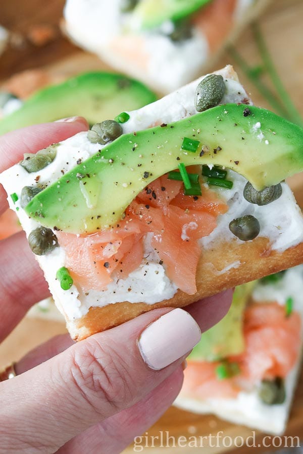 Hand holding a portion of avocado and smoked salmon flatbread appetizer.