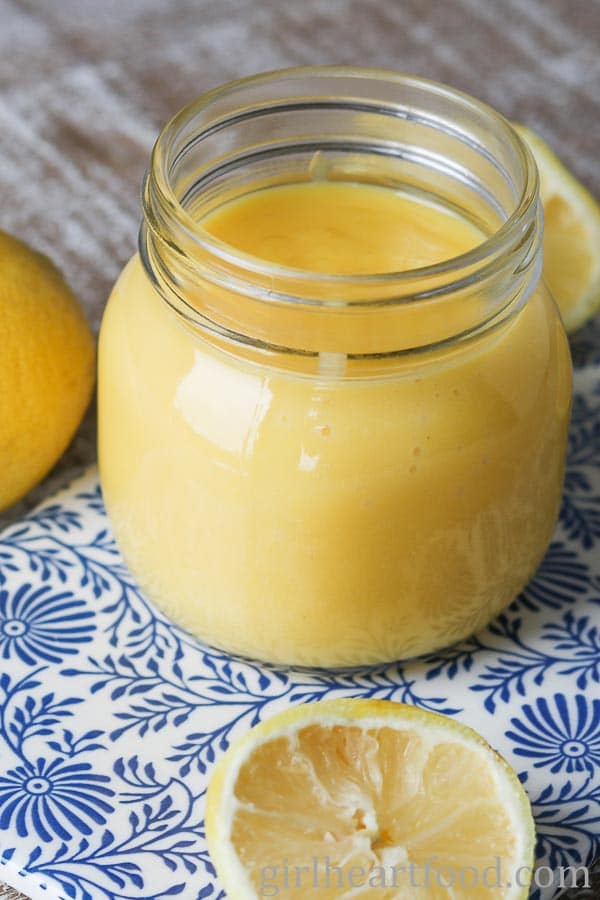 Jar of homemade lemon curd next to lemon halves.