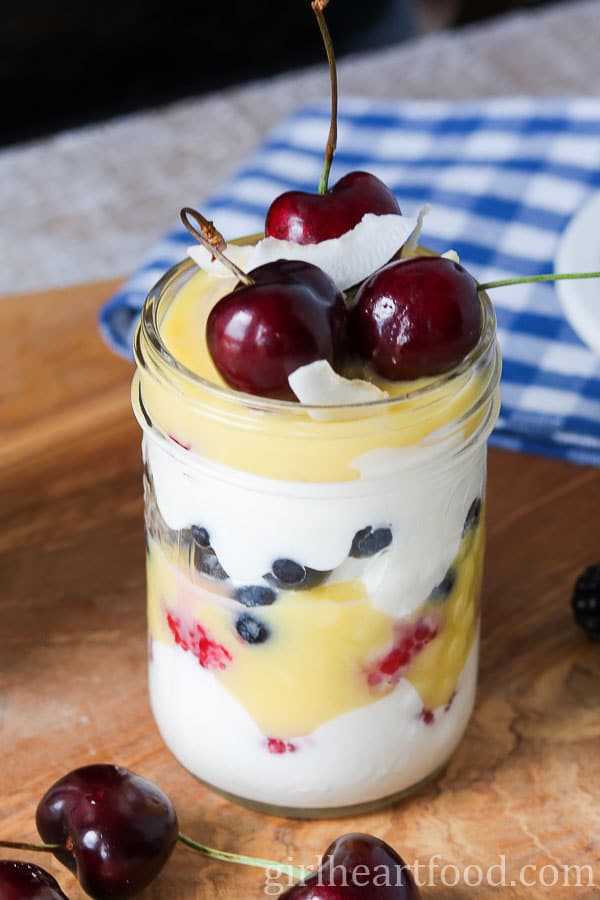 Layered dessert in a jar topped with fresh cherries and coconut.