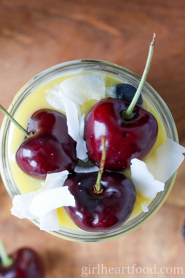 Overhead shot of dessert in a jar topped with fresh cherries and coconut.
