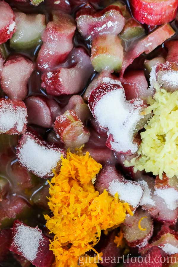 Close-up of chopped rhubarb with sugar, orange zest and grated ginger over top.