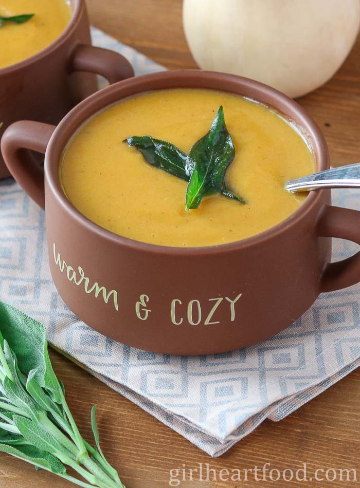 Bowl of butternut squash sweet potato soup garnished with crispy sage leaves.