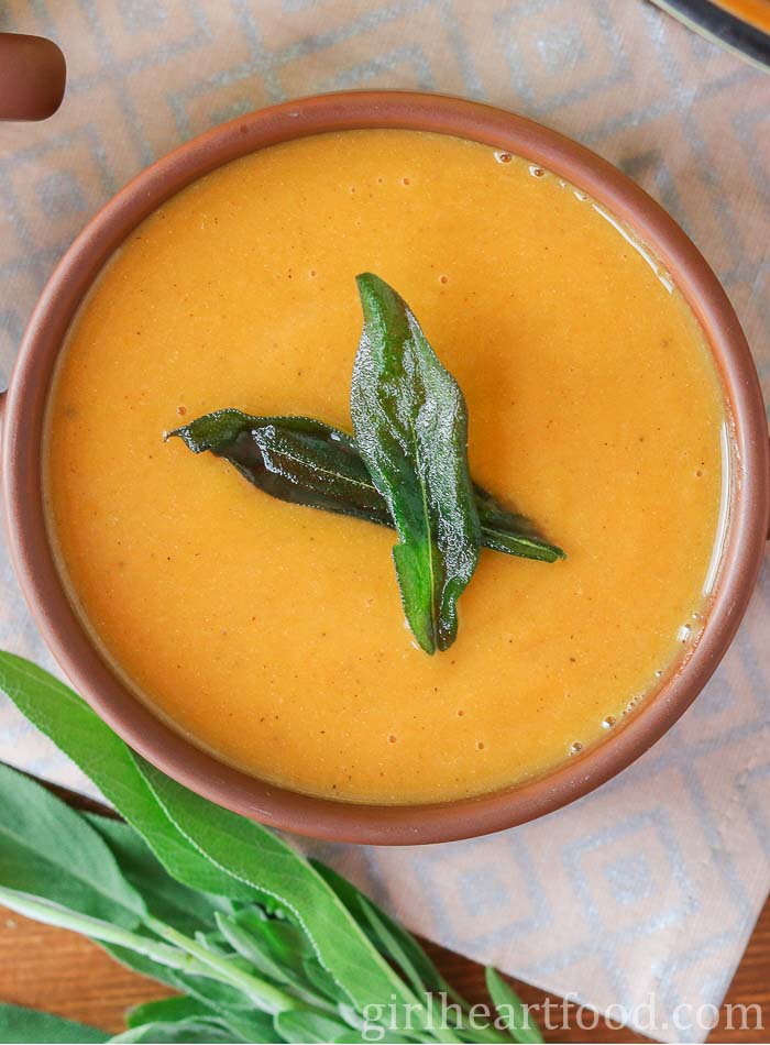 Overhead shot of a bowl of butternut squash sweet potato soup garnished with crispy sage leaves.
