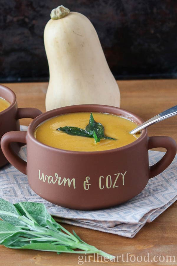 Bowl of butternut squash and sweet potato soup with a whole butternut squash behind it.