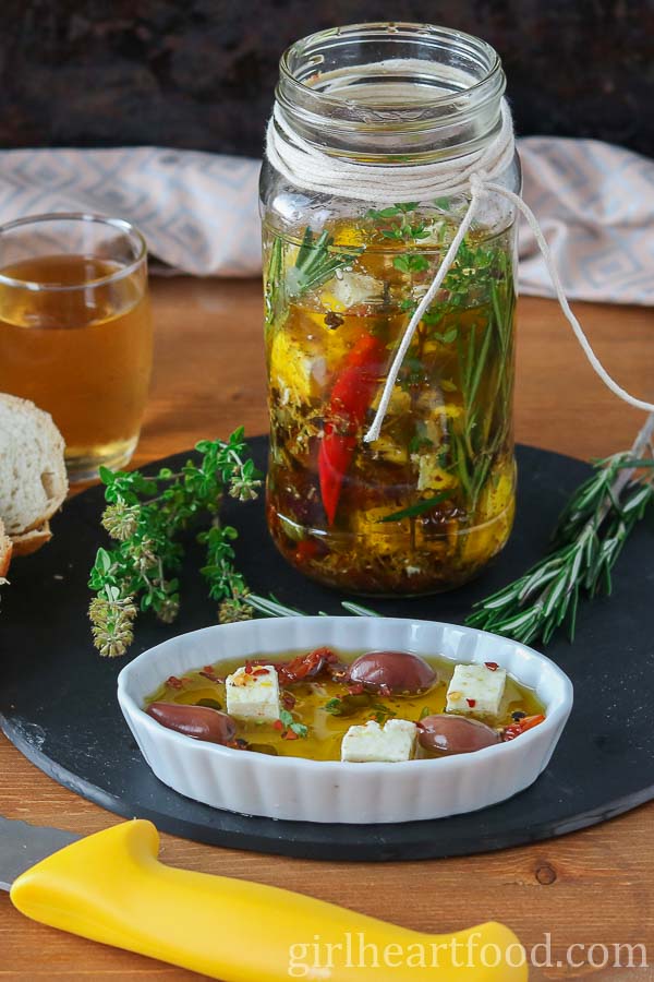 Jar of marinated feta cheese in oil with a small dish of the mixture in front of it.