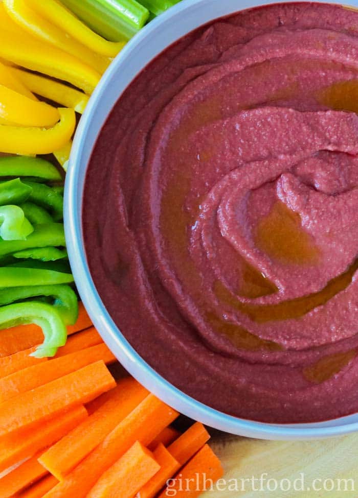 Bowl of beet cashew dip next to some veggies.