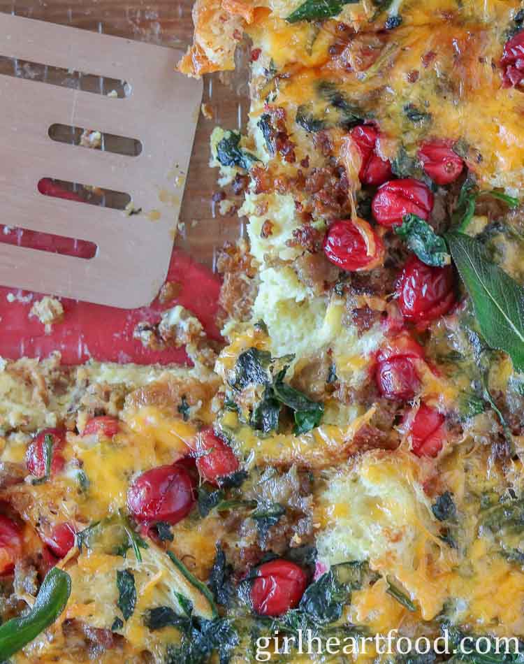 A close-up of a baking dish of breakfast strata with a spatula resting in the dish.