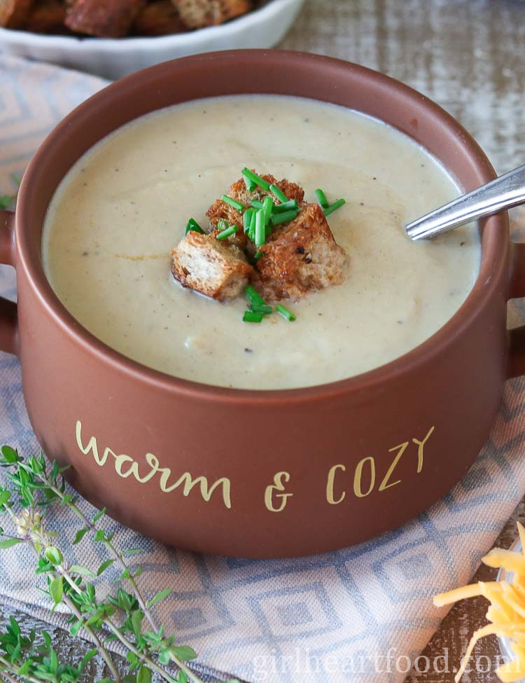 Bowl of creamy cauliflower leek soup garnished with croutons and chives.