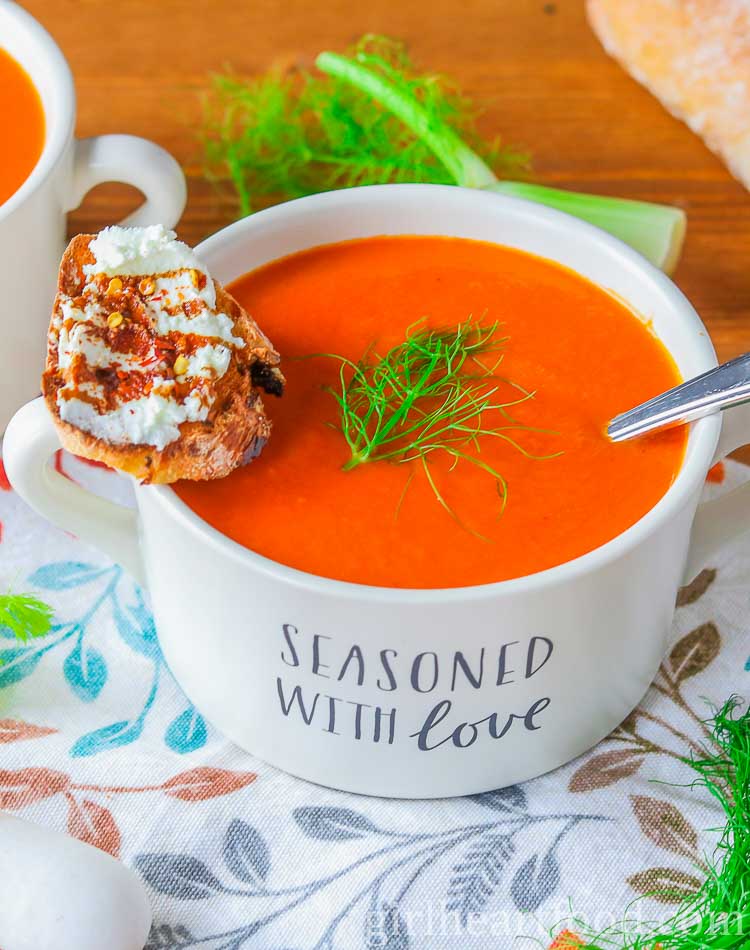 Bowl of roasted red pepper tomato fennel soup with a crostino resting on the bowl.