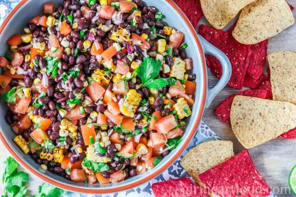 An overhead shot of a large dish of black bean and corn salsa alongside some tortilla chips.