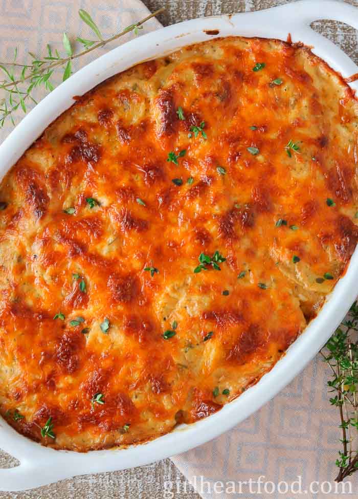 Casserole dish of cheesy scalloped potatoes garnished with thyme.