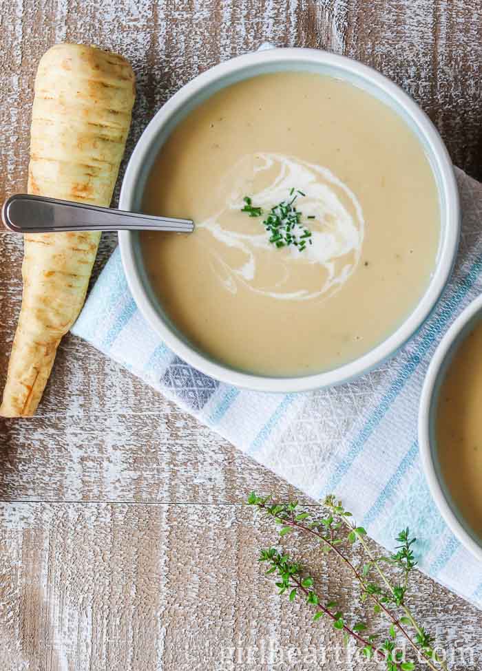 Bowl of creamy parsnip and apple soup next to a parsnip.
