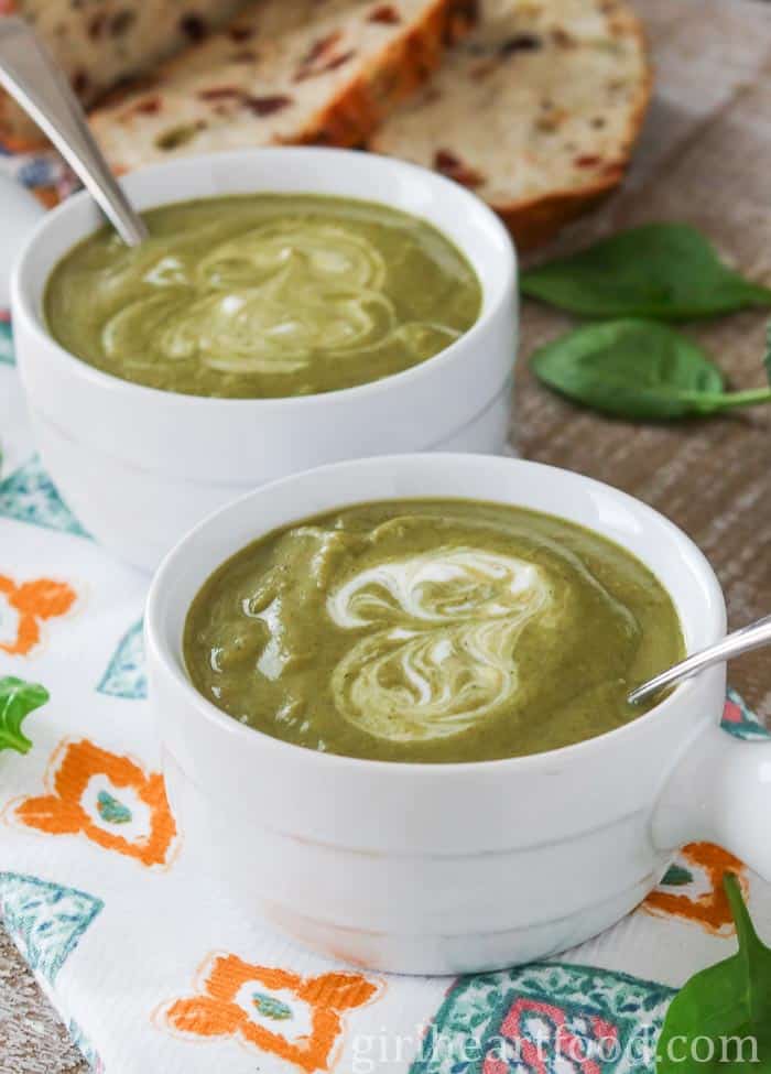 Two bowls of broccoli spinach soup with some bread behind them.