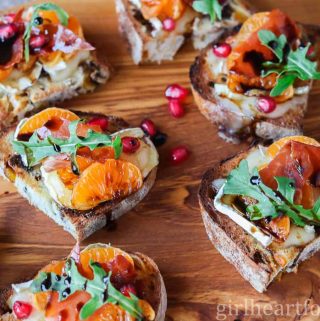 Crostini with clementine, Brie, prosciutto, arugula and balsamic on a serving board.