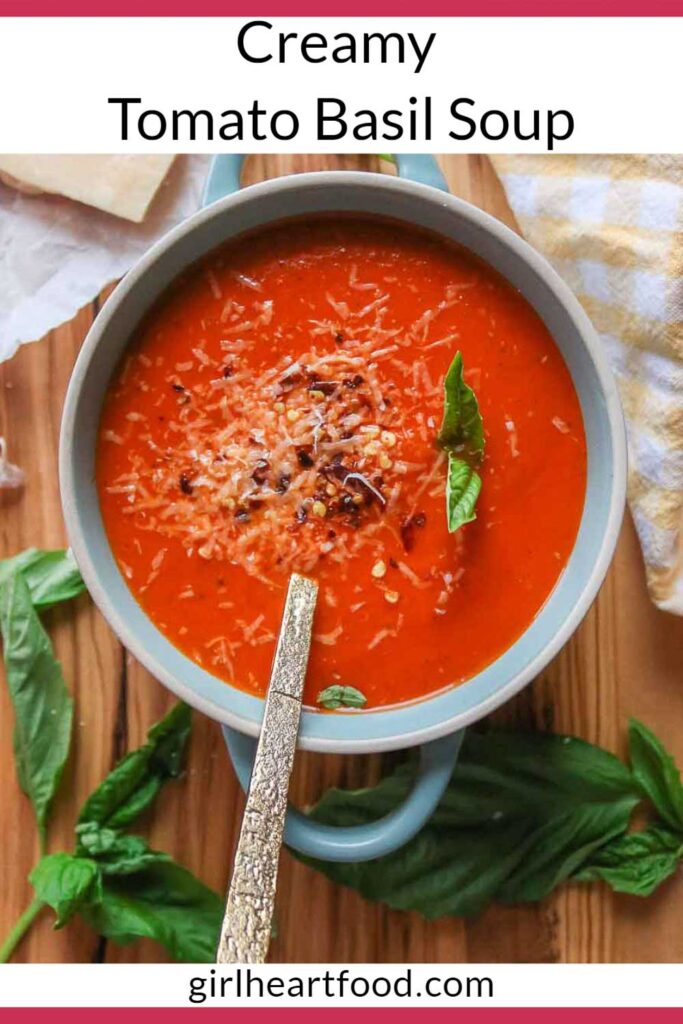 Bowl of creamy tomato basil soup garnished with cheese, red pepper flakes and basil.