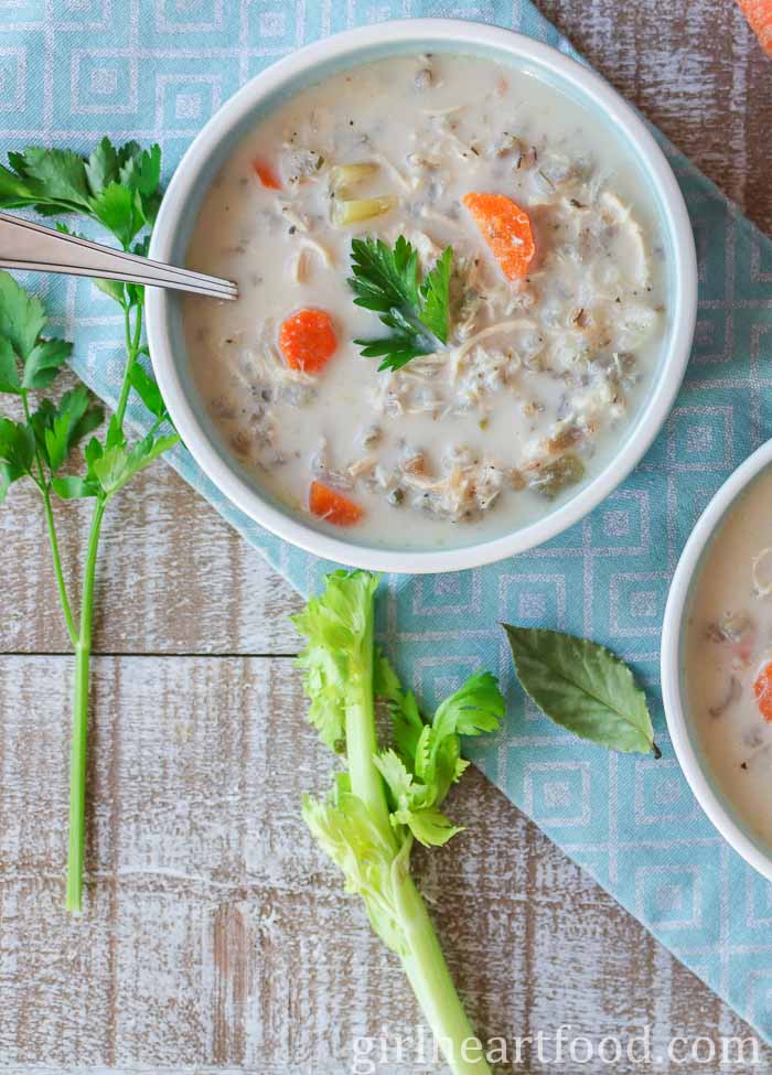 Bowl of chicken and rice soup alongside celery, parsley and a bay leaf.