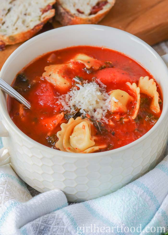 Bowl of tomato tortellini soup garnished with Parmesan cheese.