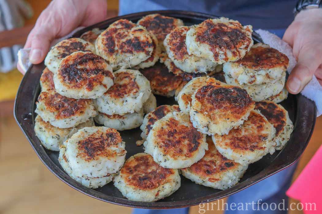Two hands holding a large tray of cooked traditional Newfoundland fish cakes.