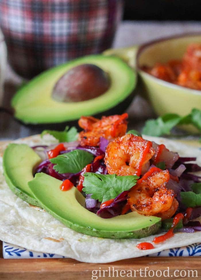 Shrimp taco garnished with toppings, sitting in front of half an avocado.