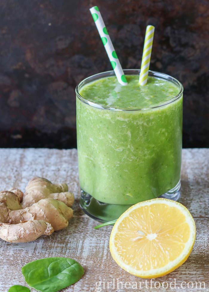 Glass of a ginger smoothie alongside lemon, ginger and spinach.
