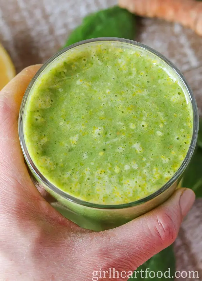 Hånd med et glas grøn ingefær-smoothie i hånden.