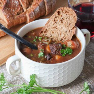Bowl of moose stew with a slice of bread and spoon dunked into it.