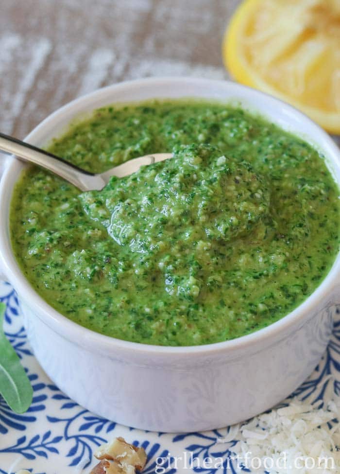 Arugula pesto in a small white bowl with a spoon dunked into it.