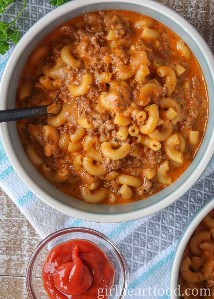 Bowl of cheeseburger macaroni next to a dish of ketchup.