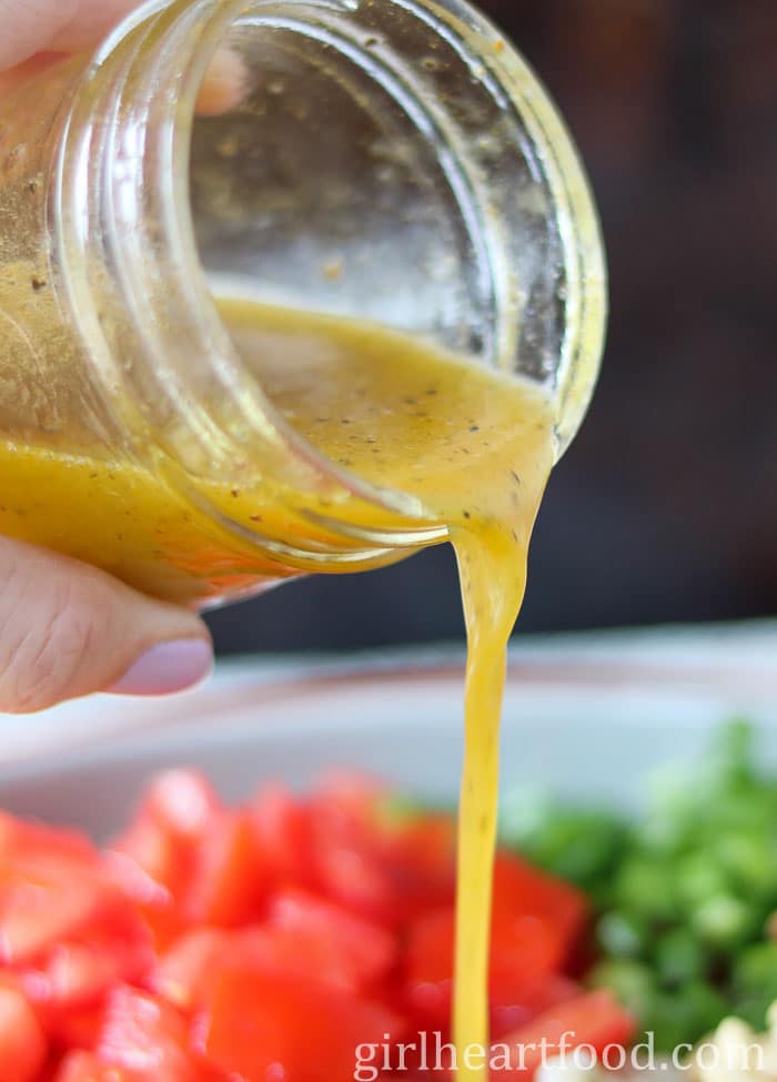 Hand holding a jar of lemon turmeric dressing, pouring it over a salad. 