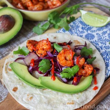 Shrimp taco with garnish, next to a lime wedge.