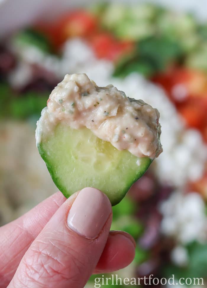 Hand holding a slice of cucumber that has been dipped in bean dip.