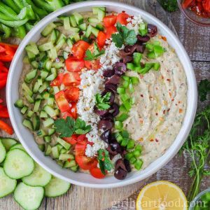 White bowl of Mediterranean white bean dip alongside veggies, lemon and parsley.