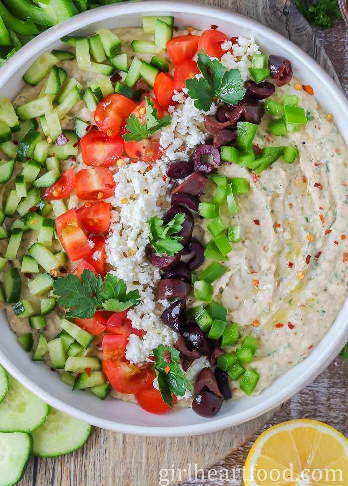 Bowl of Mediterranean white bean dip garnished with toppings.