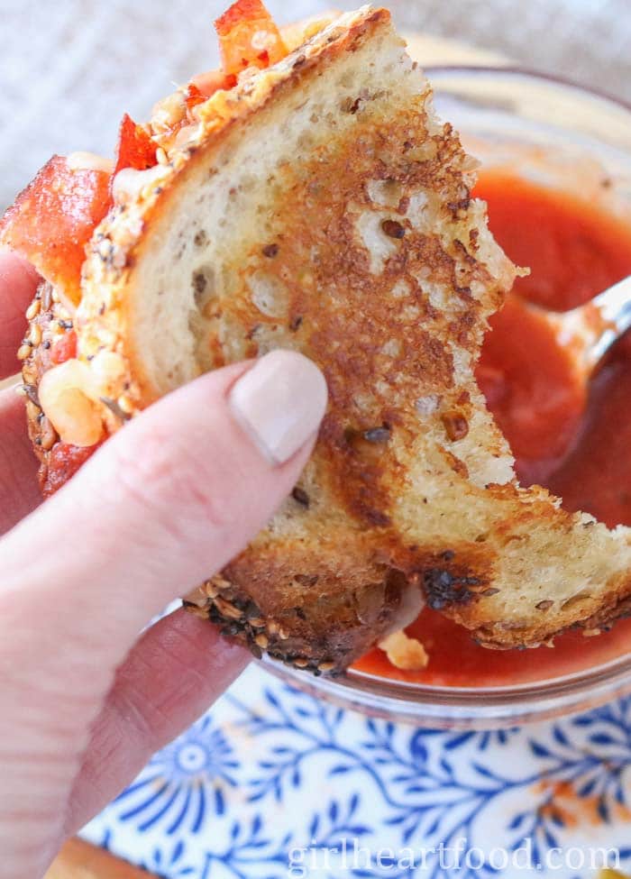 Hand dunking a grilled pizza sandwich into pizza sauce.