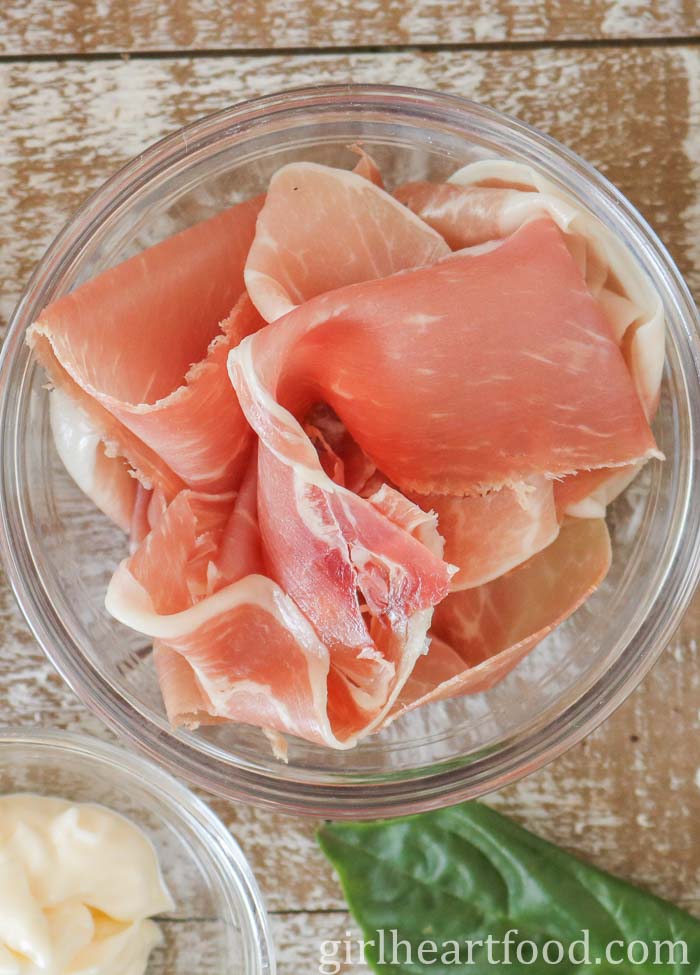 Slices of prosciutto in a small clear bowl.