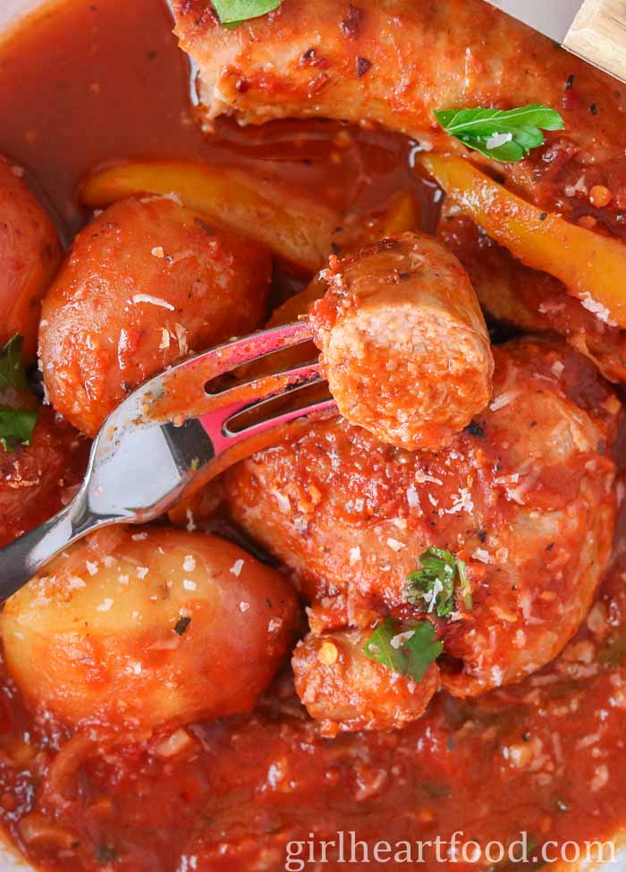 Fork piercing a chunk of sausage covered in tomato sauce, resting on a chicken thigh.