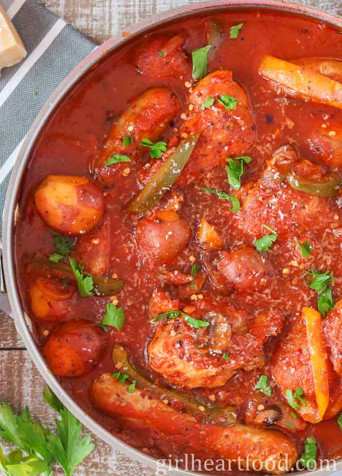 Close-up of a pan of chicken, sausage, peppers and potatoes in tomato sauce.