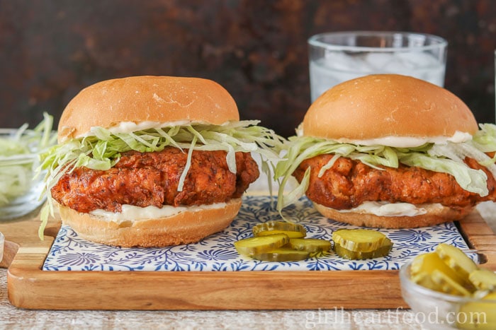 Two crispy chicken sandwiches, each with mayo and lettuce, next to some sliced pickle.