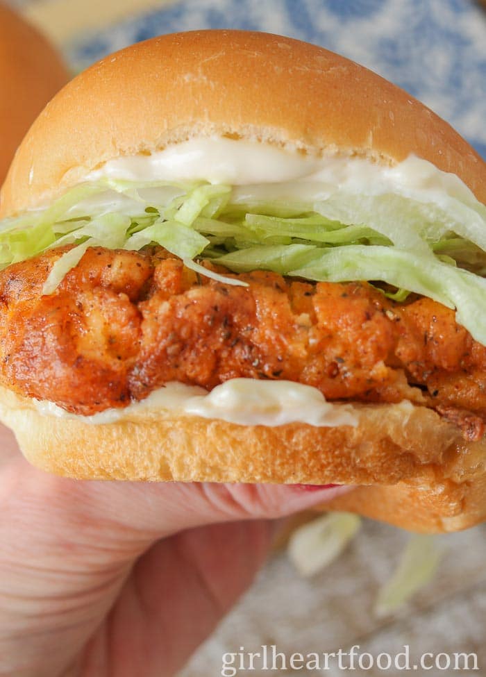 Hand holding a fried chicken burger with mayo and lettuce.