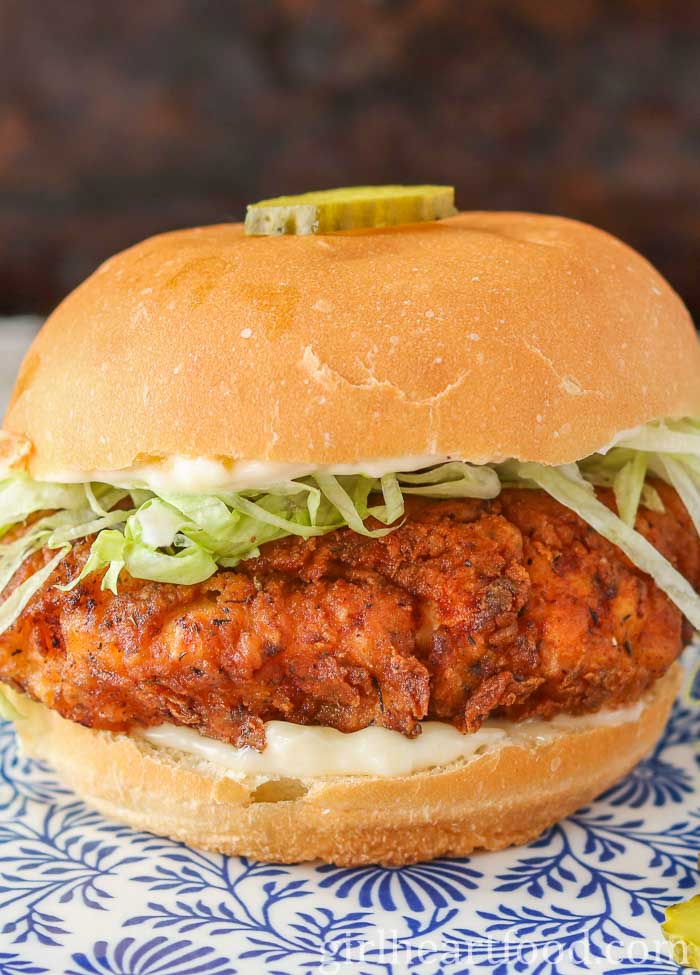 Fried chicken sandwich with mayo and lettuce and a pickle slice on top of the bun.