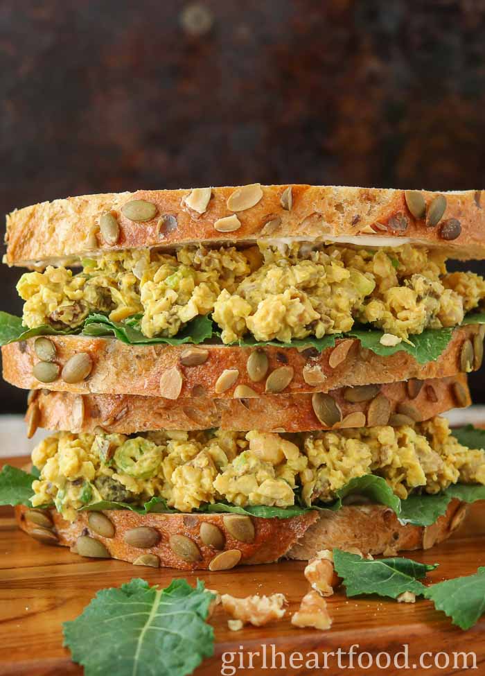Close-up of a stack of two chickpea salad sandwiches next to baby kale and walnuts.