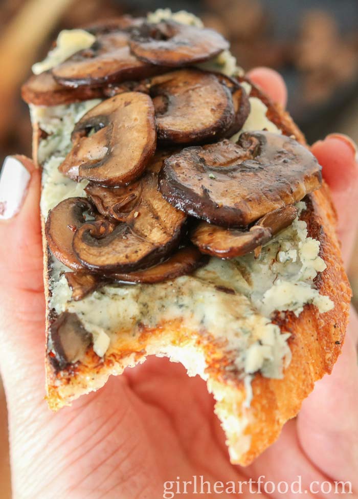 Hand holding a piece of toast topped with blue cheese and mushrooms.
