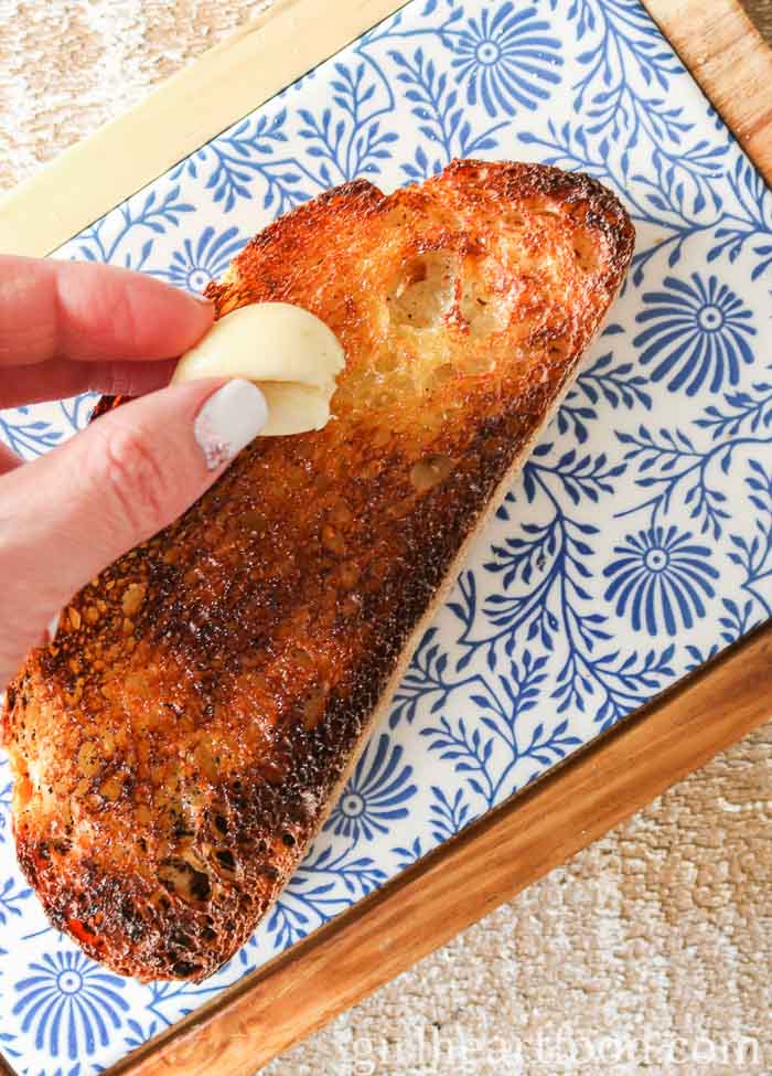 Hand rubbing a garlic clove over a piece of toast.